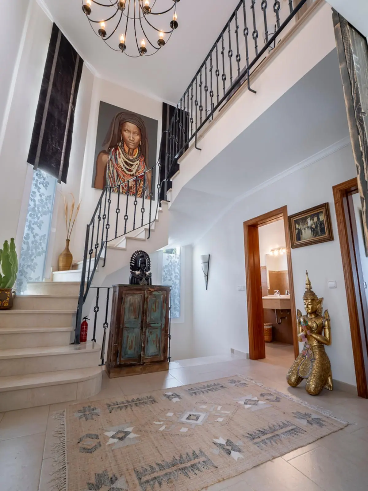 Entrance hall featuring a marble staircase with wrought-iron railings, a large wall portrait, a golden statue, and an eclectic patterned rug.