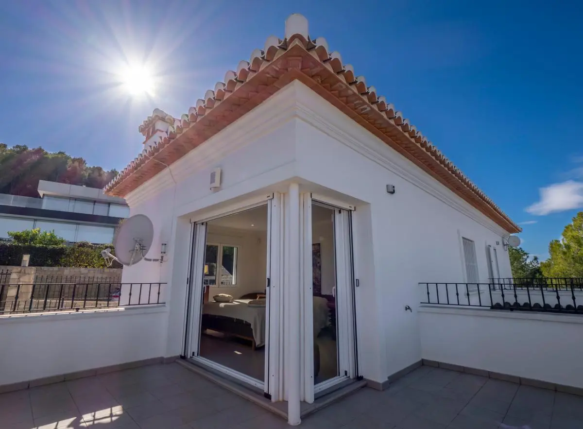 Exterior view of an upper-floor bedroom featuring large sliding glass doors that open onto a private, tiled terrace under a traditional terracotta roof.