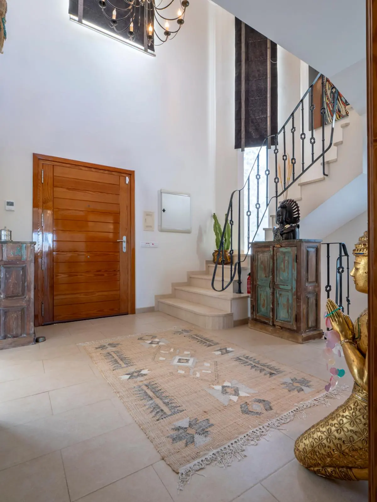 Foyer with a solid wood entrance door, stone staircase with wrought iron railings, and a classic chandelier. Rustic decor and tiled flooring define the space.