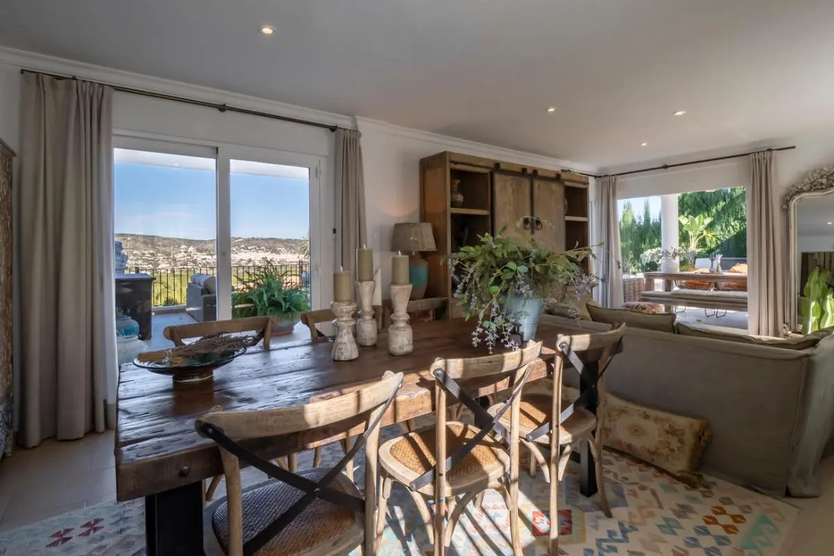 Rustic dining area featuring a solid wood table and cross-back chairs, with sliding glass doors opening to a terrace overlooking the valley.