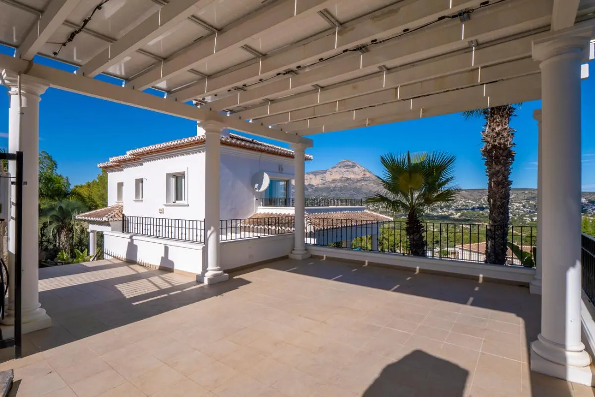 Spacious covered terrace with white columns and a pergola roof, offering views of the Montgó mountain and the surrounding Mediterranean landscape.