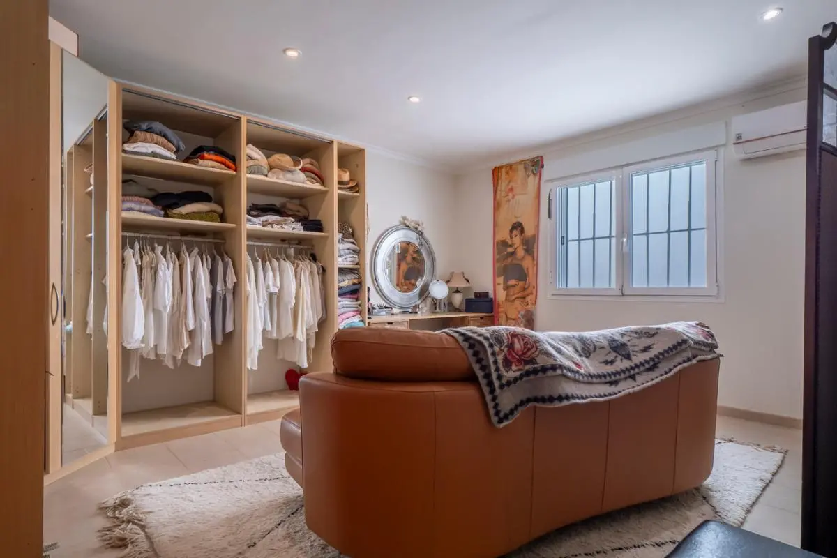 Spacious dressing area featuring an open wooden wardrobe system, a tan leather sofa, and a dedicated vanity station with a circular mirror.