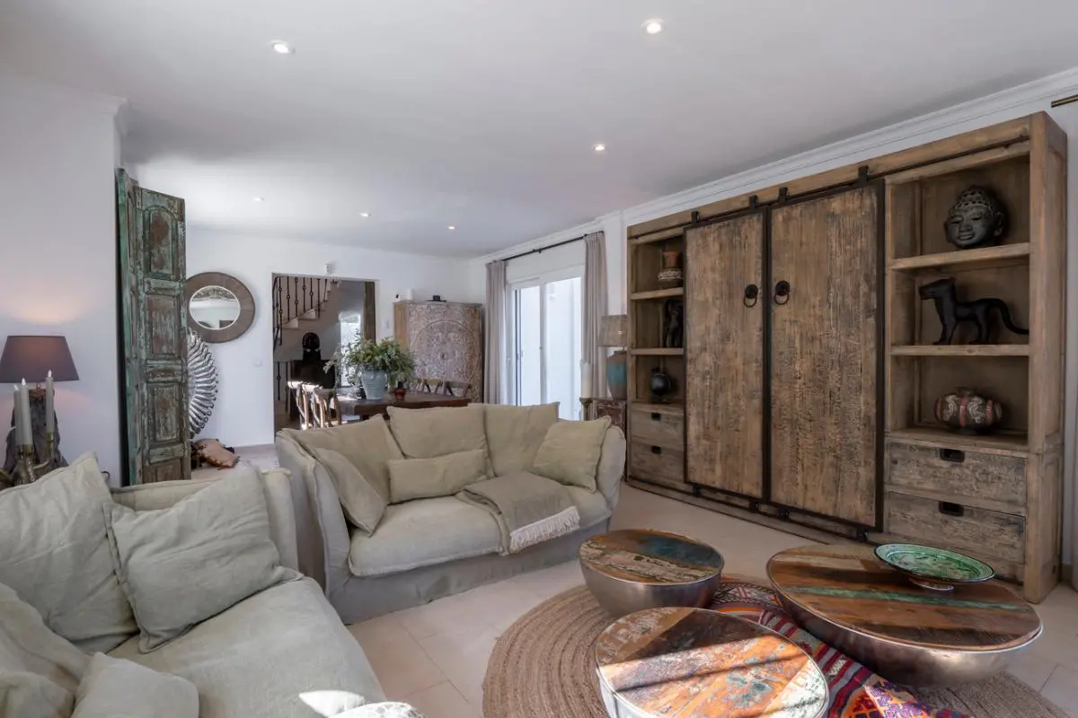 Spacious living area with a large rustic wooden wall unit, beige linen-covered sofas, and reclaimed wood coffee tables on a circular jute rug.