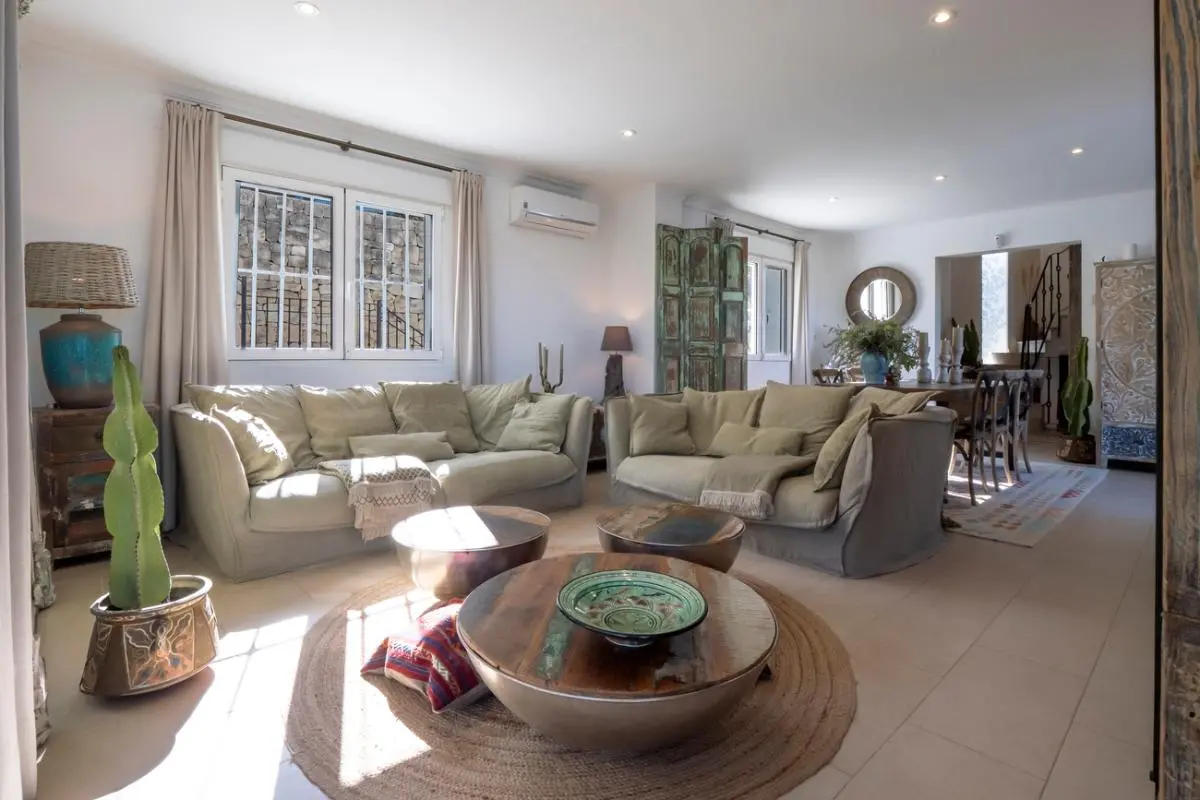 Spacious living room featuring neutral sofas, circular wooden coffee tables on a jute rug, and rustic decor with natural light and recessed lighting.