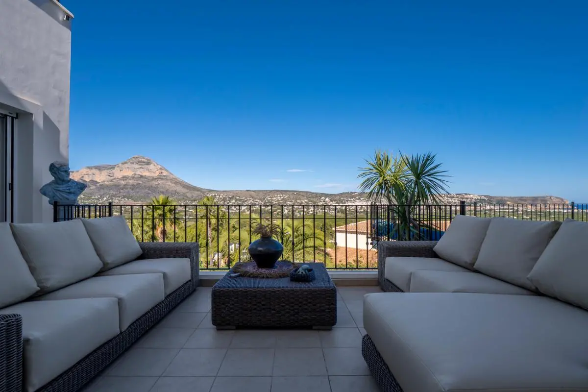 Terrace lounge featuring grey wicker seating and a central table, offering panoramic views of the Montgó mountain and the valley.