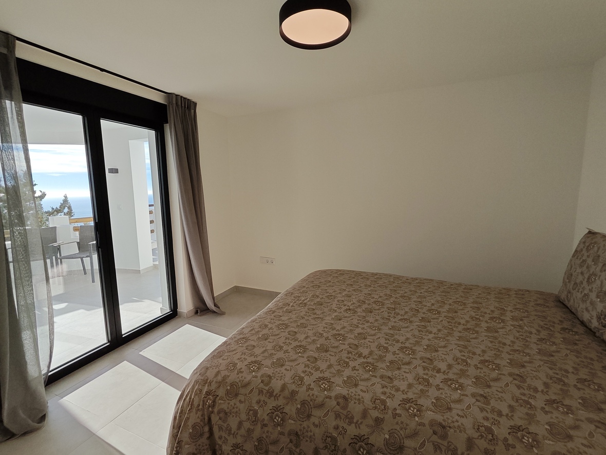 Bedroom featuring a double bed with floral textiles and direct access to a private terrace through sliding glass doors, offering sea views.