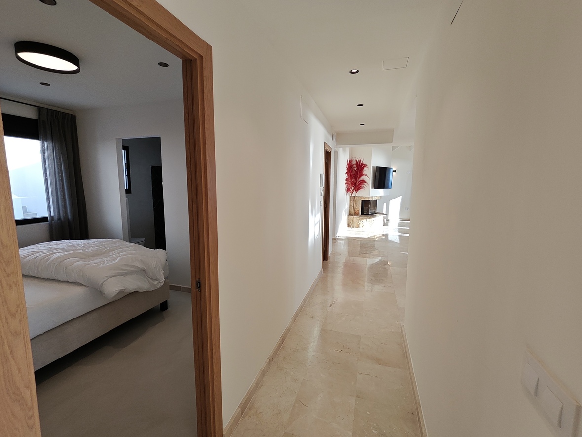 Bright hallway with polished marble flooring leading to a living area with a stone fireplace, featuring a side view into a bedroom.