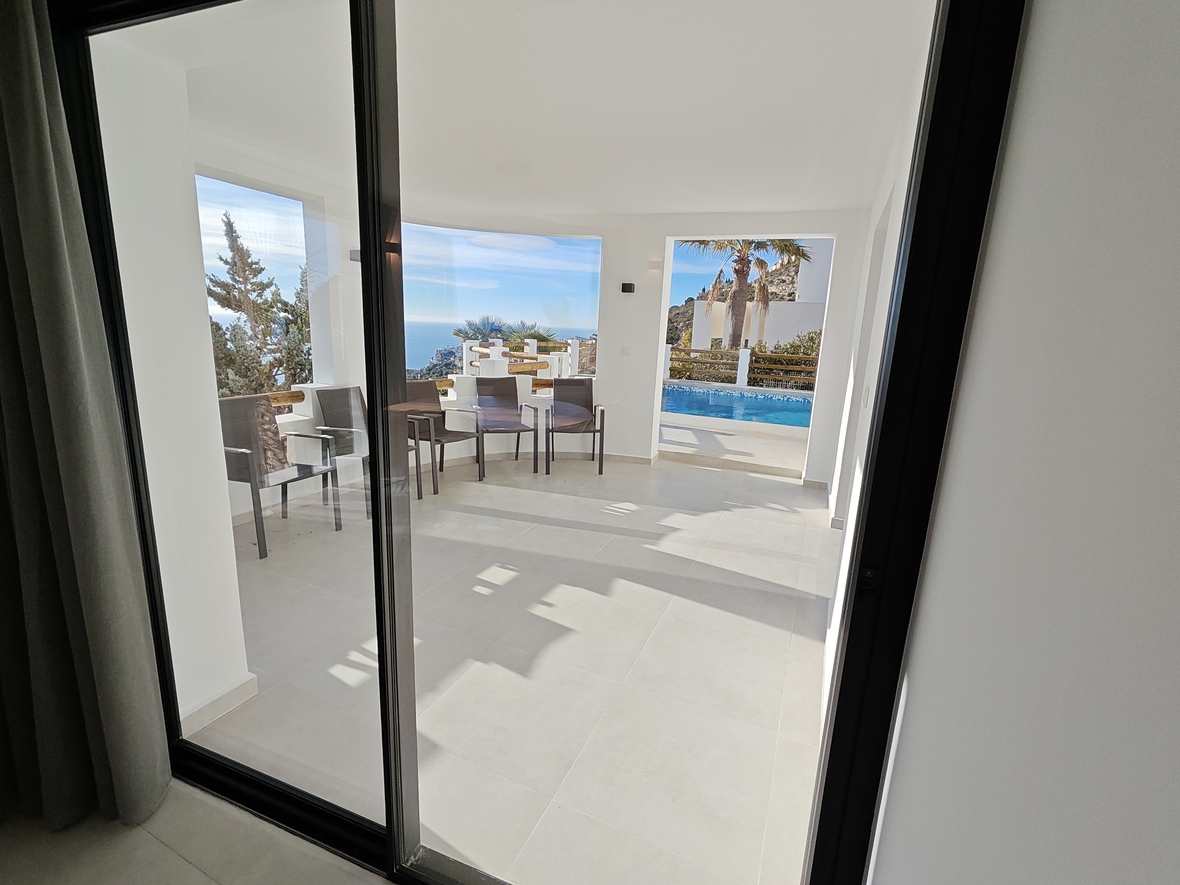 Covered terrace featuring white tiled flooring and outdoor seating, with expansive views of the sea and the adjacent private swimming pool.