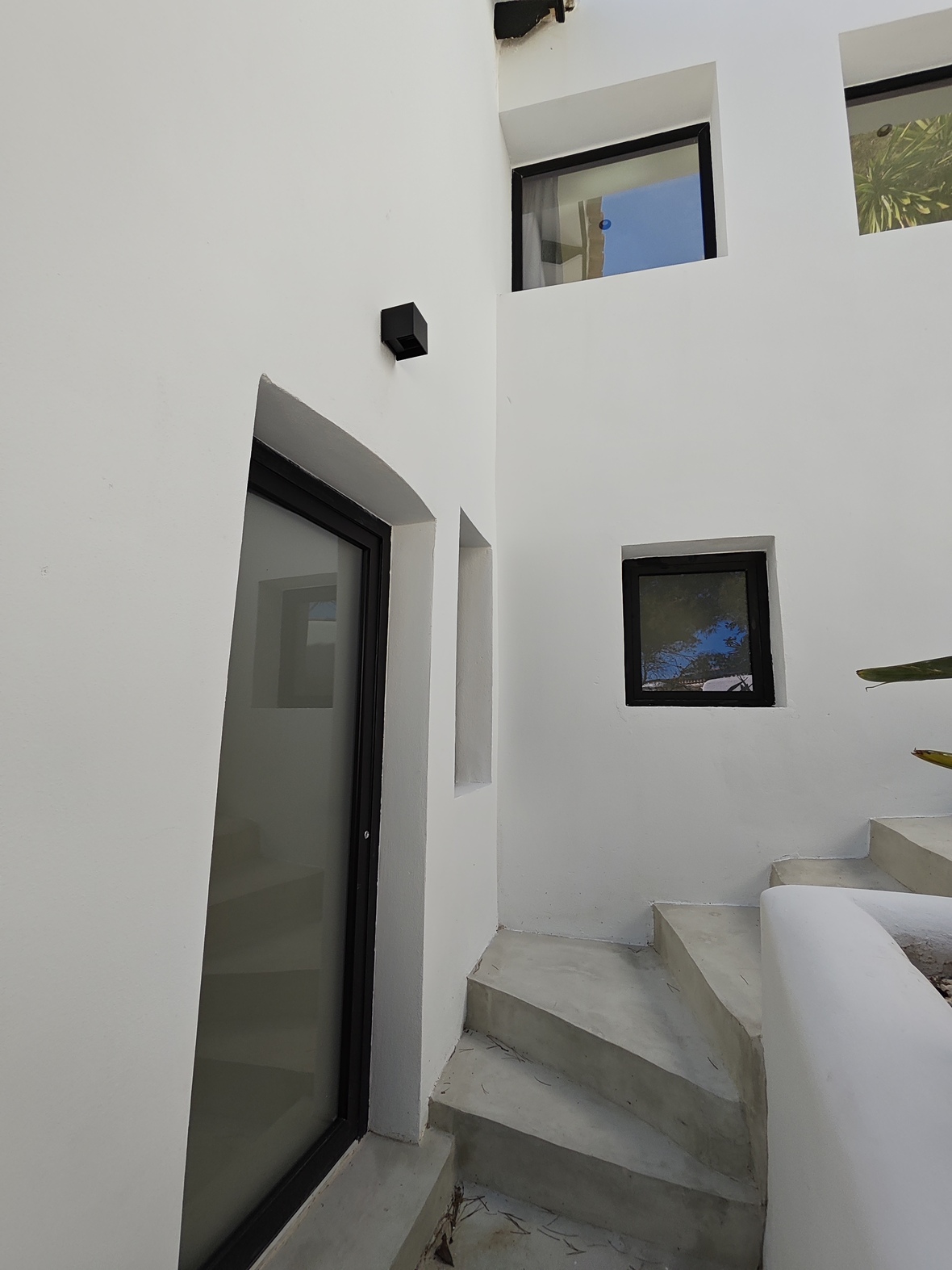 Exterior concrete staircase set against minimalist white walls, featuring black-framed windows and a frosted glass entry door.
