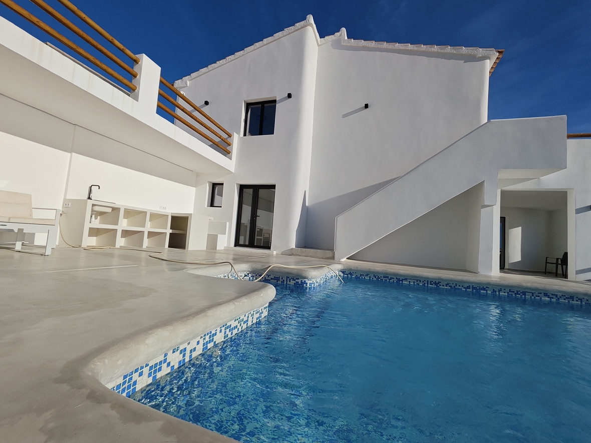 Exterior terrace featuring a private pool with blue mosaic tiling, an outdoor kitchenette, and a minimalist white facade with wooden railings.