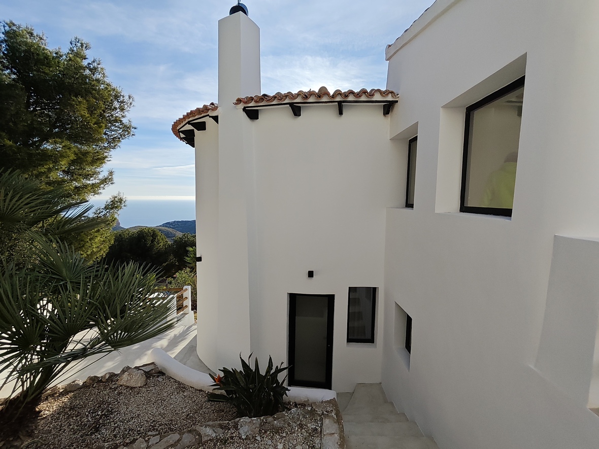 Exterior view of a white Mediterranean villa featuring a curved facade, terracotta roof tiles, and concrete stairs leading to an entrance with sea views.