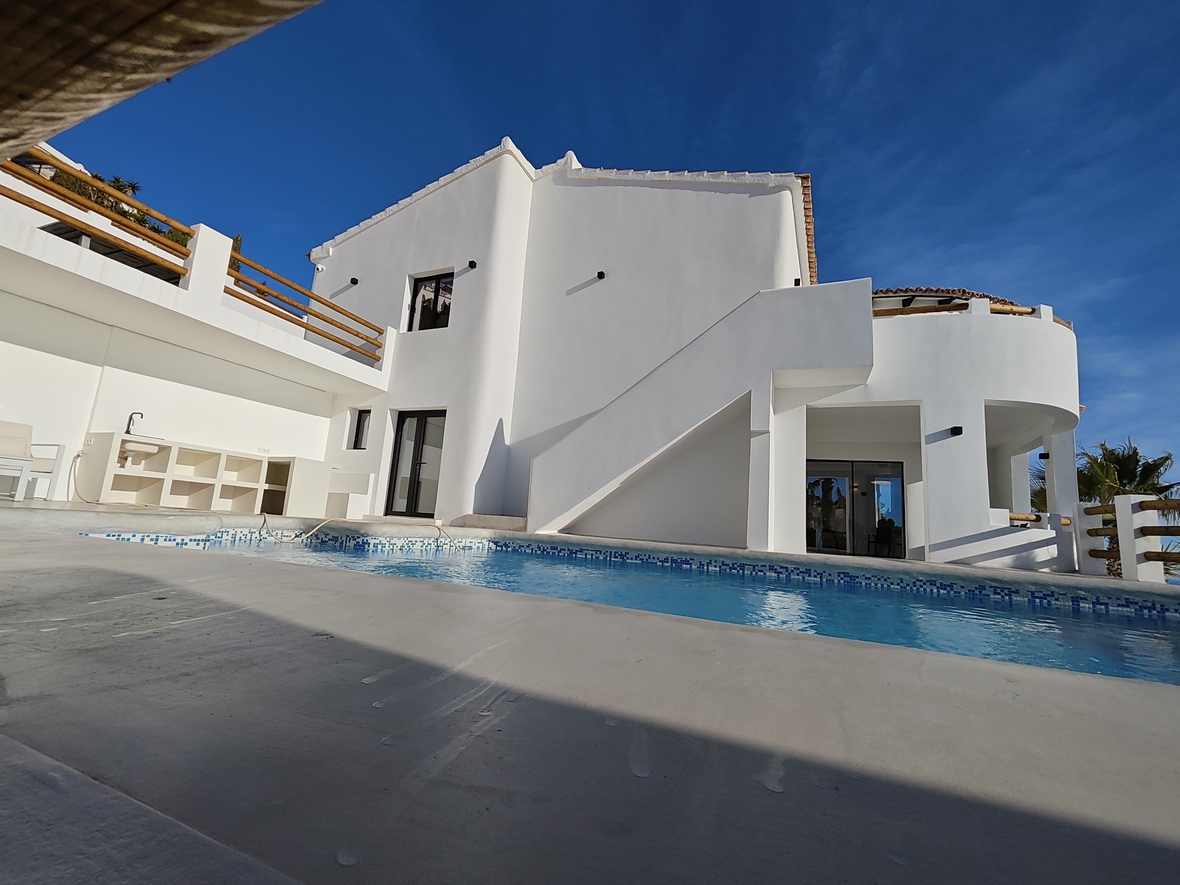 Exterior view of a white multi-level villa featuring a private pool with blue tiles, integrated outdoor kitchen, and wooden railings.