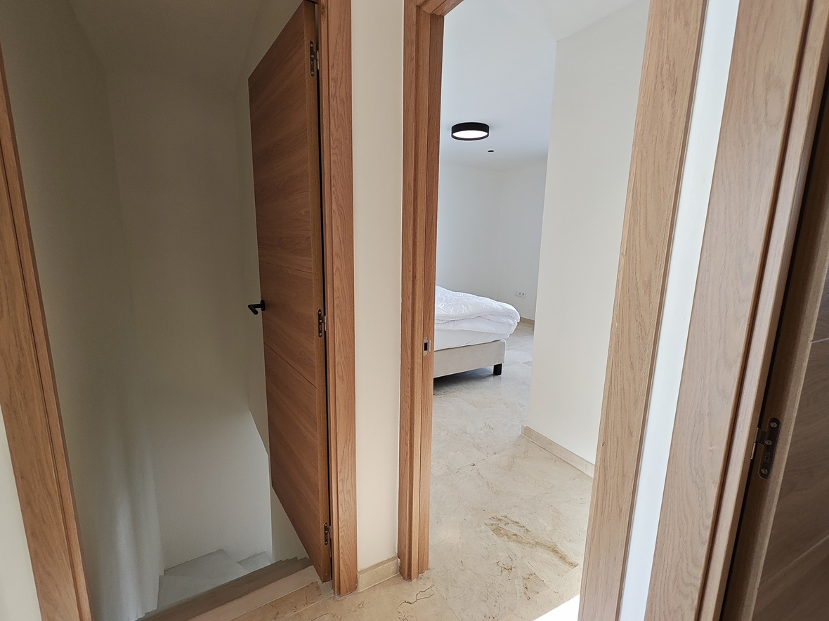 Hallway landing featuring oak-finished doors and stone flooring, providing access to a bedroom and a staircase leading to the lower level.