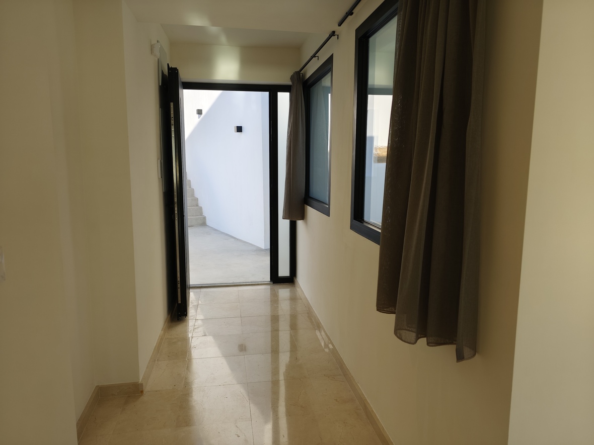 Hallway with polished marble flooring providing access to an outdoor courtyard with stone stairs. Features black-framed glazing and neutral curtains.