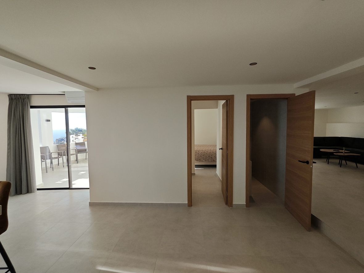 Interior hallway featuring light stone-effect tiling, natural wood doors, and a sliding glass exit to a terrace overlooking the ocean.