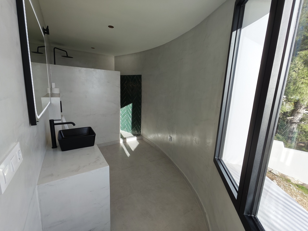 Minimalist bathroom featuring curved microcement walls, a black vessel sink, and a walk-in shower with green herringbone tile accents.