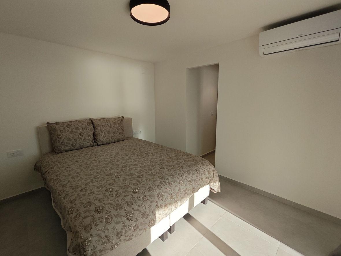 Minimalist bedroom featuring a double bed with floral patterned linens, split-system air conditioning, and a circular black ceiling light.