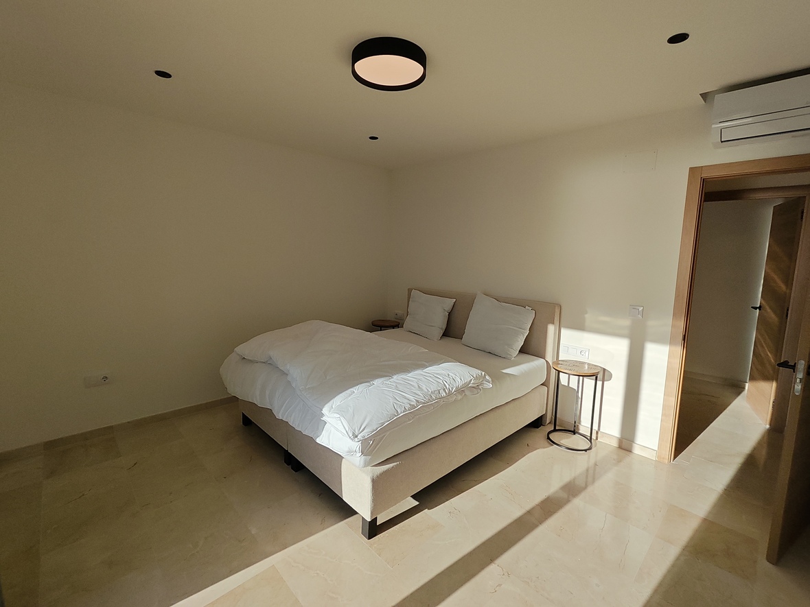 Minimalist bedroom featuring polished stone flooring, an upholstered double bed, and modern lighting including a circular ceiling fixture and recessed spotlights.
