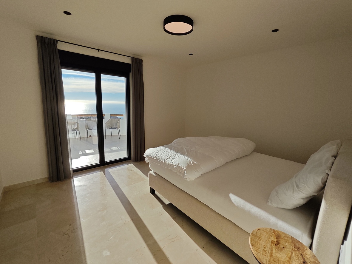 Modern bedroom featuring polished marble floors, a double bed, and sliding glass doors leading to a terrace with expansive sea views.