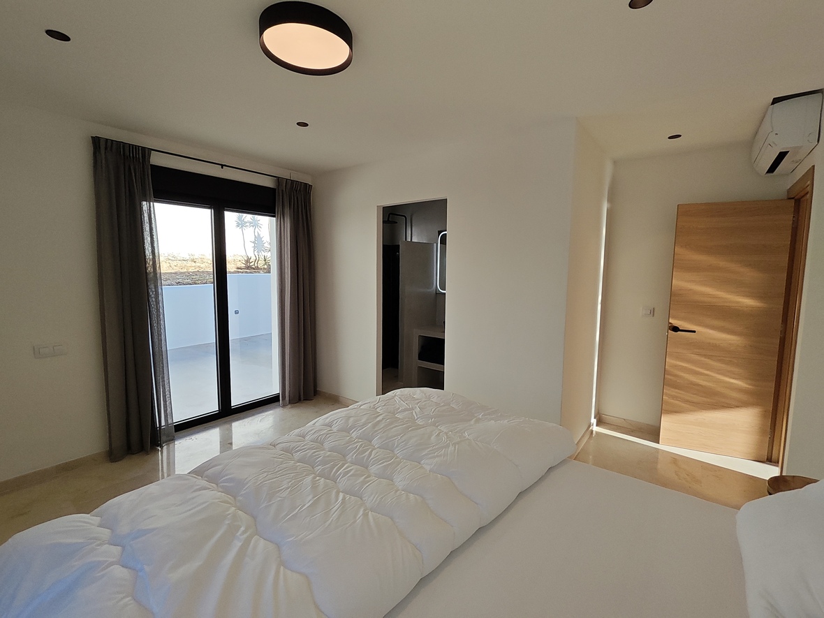Modern bedroom featuring polished stone floors, private terrace access via sliding doors, and an integrated en-suite bathroom.