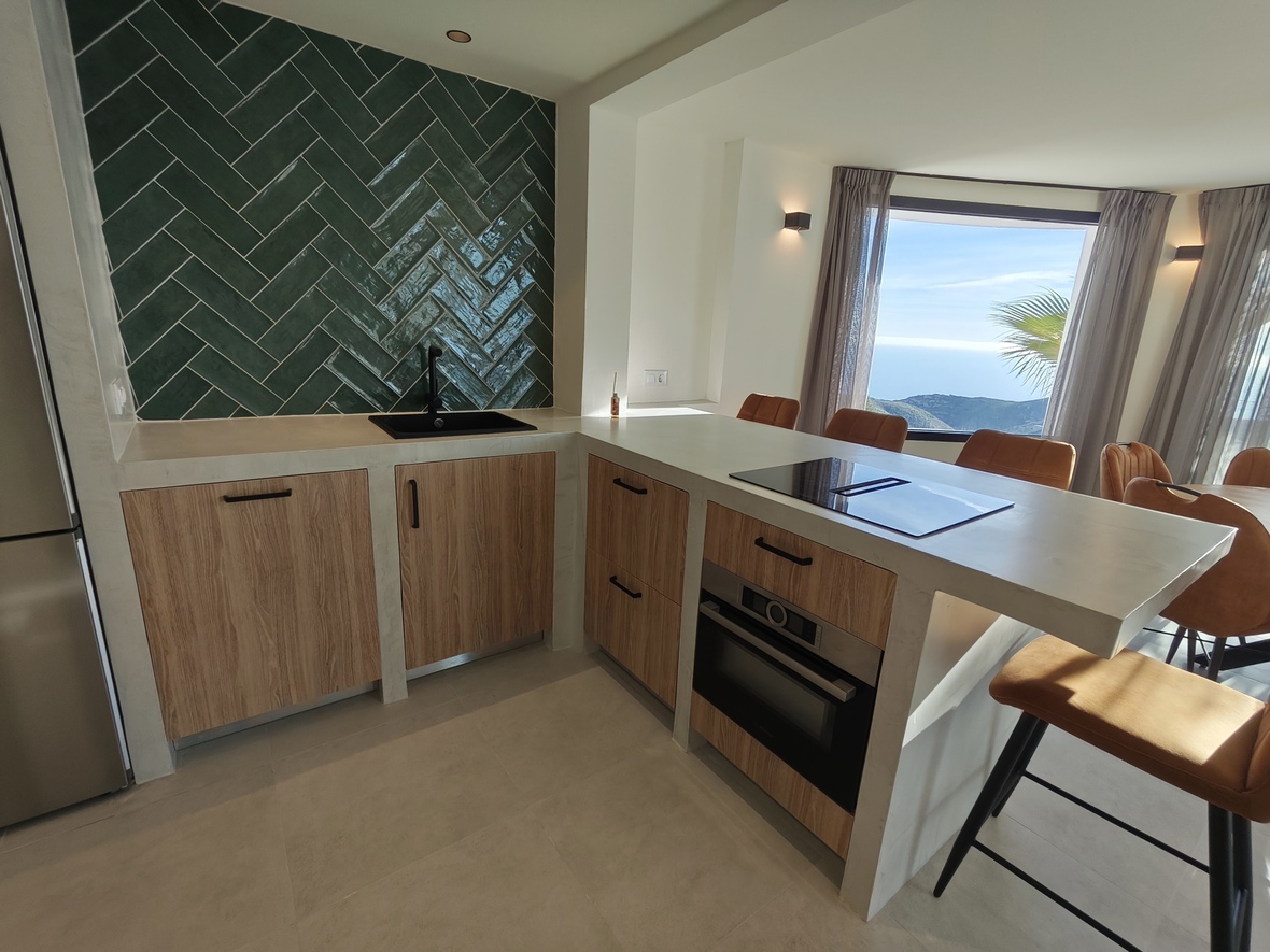 Modern kitchen featuring a green herringbone backsplash, wooden cabinetry, and an island with an integrated cooktop and panoramic sea views.