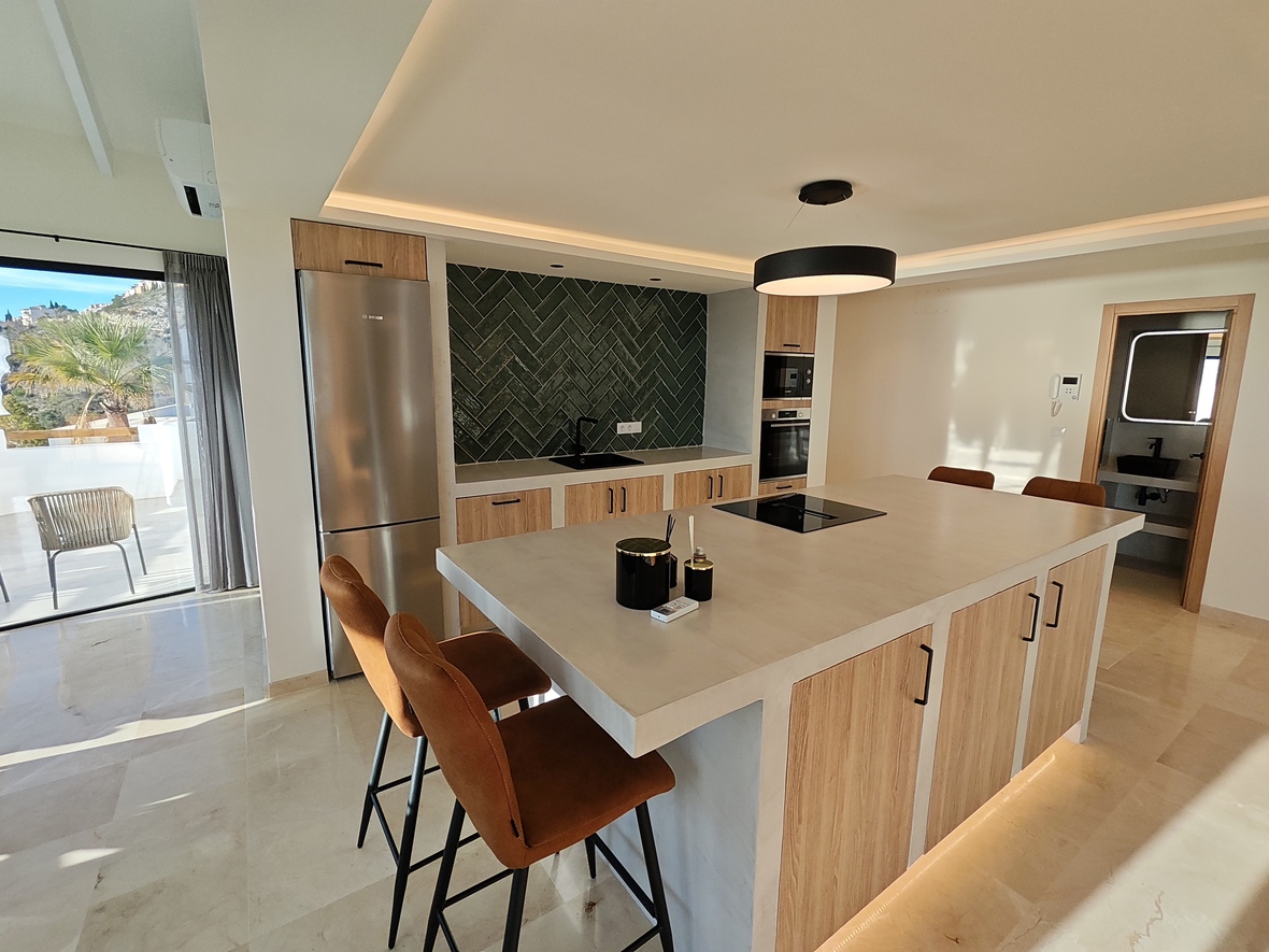Modern kitchen featuring a large island with stone countertop, leather stools, and a dark green herringbone tile backsplash. Includes integrated appliances and terrace access.