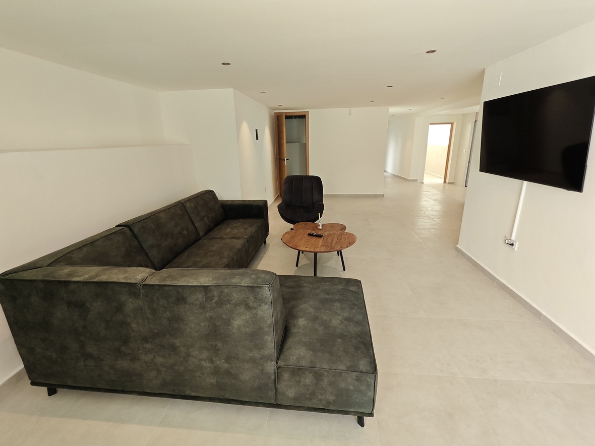 Modern living space featuring a dark green L-shaped sofa, natural wood coffee table, and wall-mounted flat-screen TV with recessed ceiling lighting.