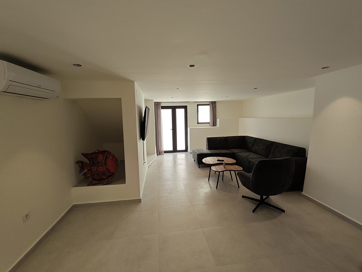 Modern living space with a dark grey sectional sofa, organic wooden tables, and a decorative wall niche. Features recessed lighting, air conditioning, and tiled flooring.