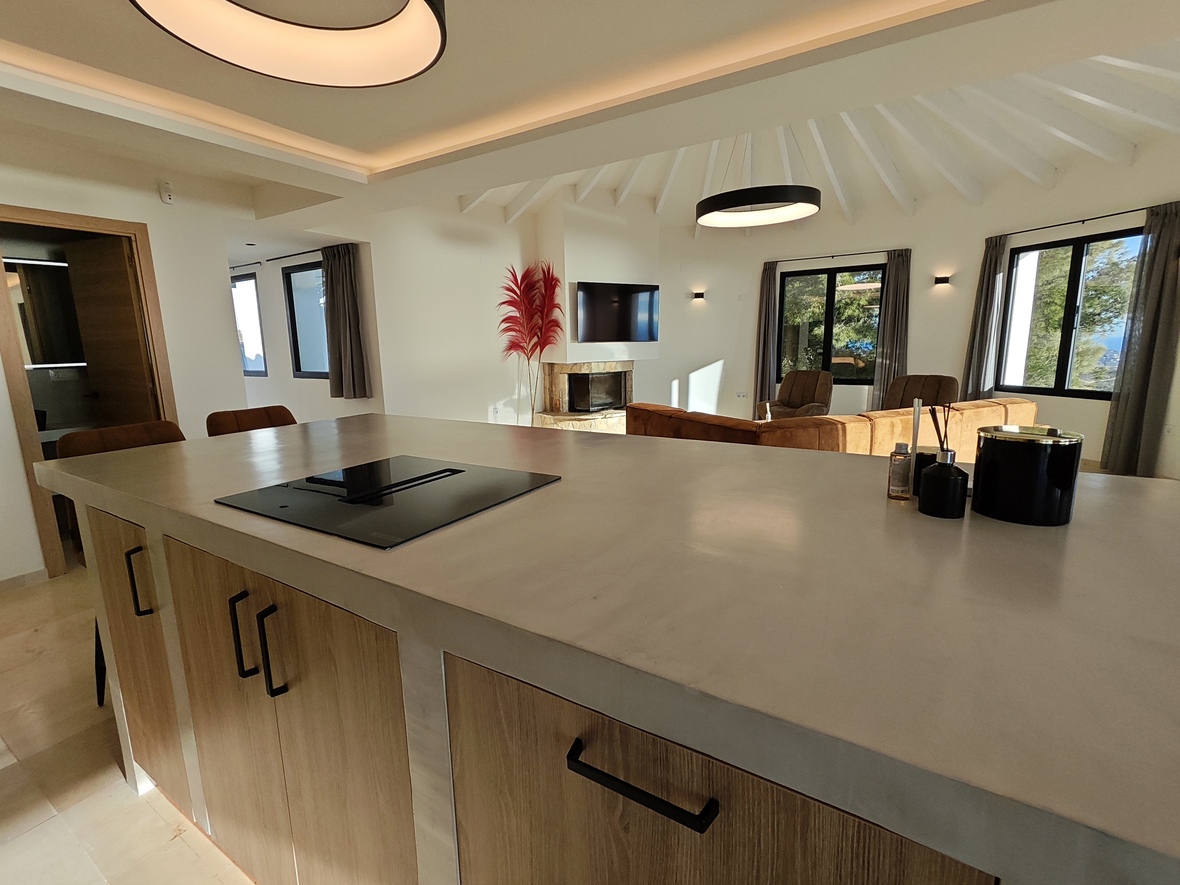 Modern open-plan kitchen featuring a stone-top island with integrated induction hob, leading to a living area with vaulted beamed ceilings and a stone fireplace.