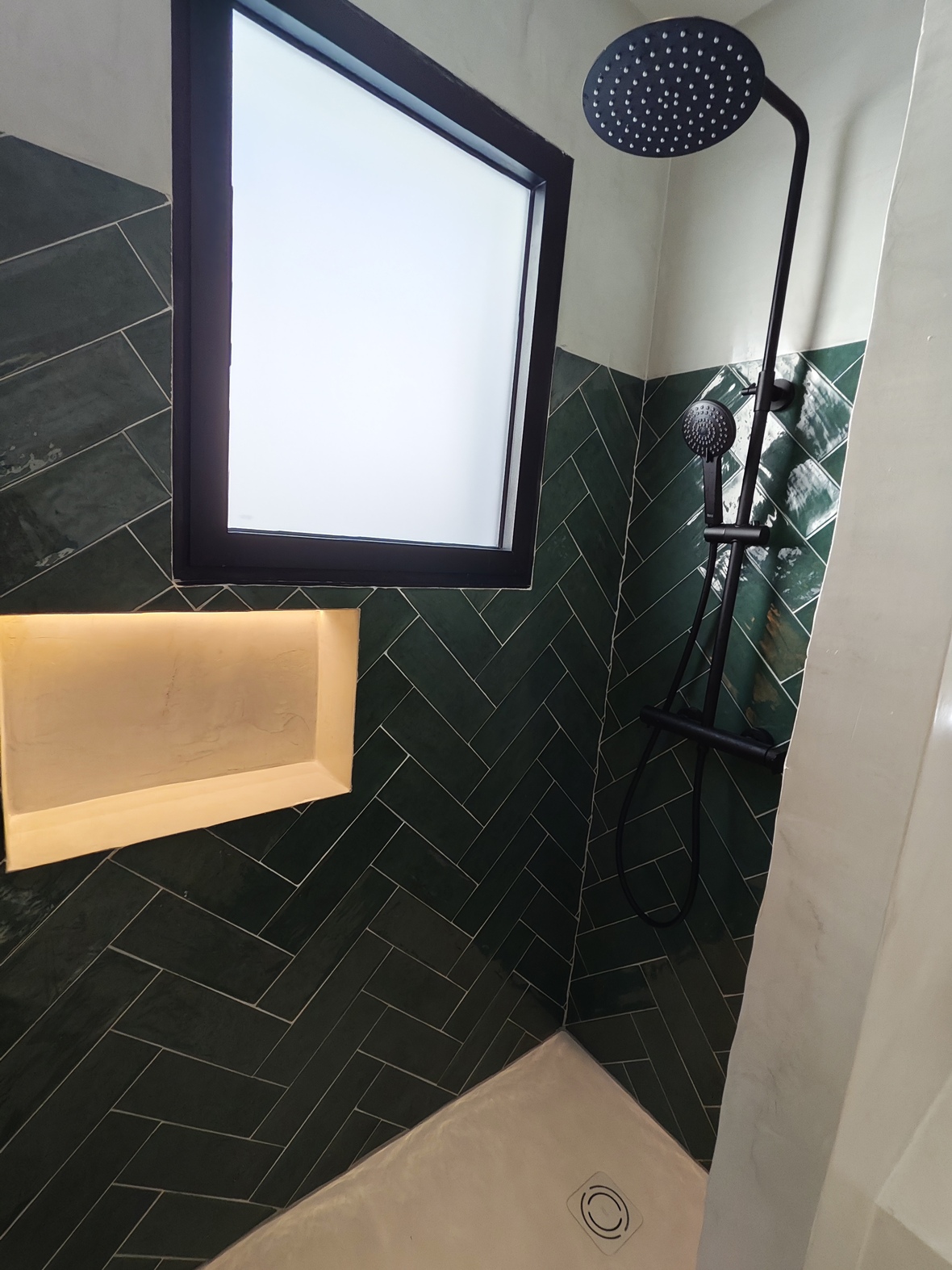 Modern shower featuring dark green herringbone tiling, matte black fixtures, a recessed illuminated niche, and a frosted window for privacy and natural light.