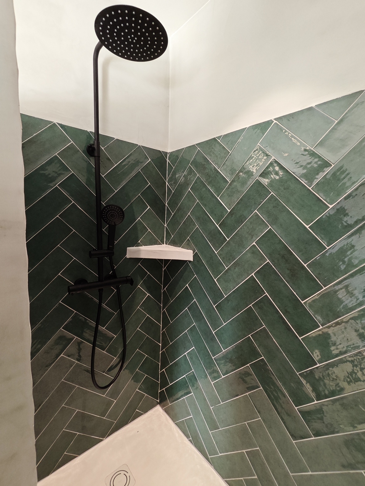 Modern shower featuring emerald green subway tiles in a herringbone pattern, matte black fixtures, and a large rain shower head.