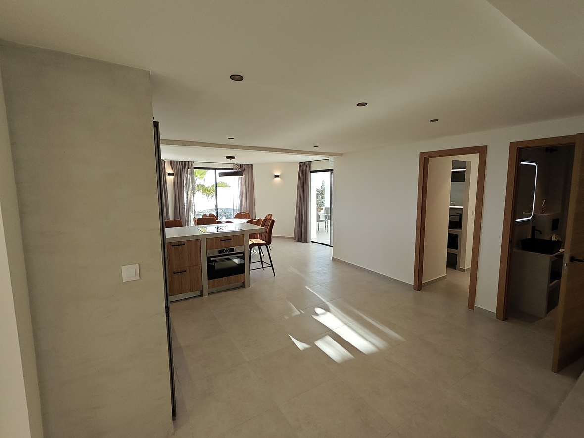 Open-plan living area featuring a kitchen island with wood finishes, integrated oven, and recessed lighting over neutral tiled floors.