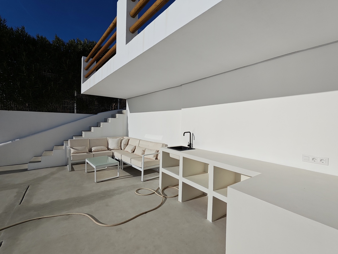 Outdoor terrace featuring a built-in masonry kitchen with a black sink, adjacent to a lounge area with an L-shaped sofa and glass table.