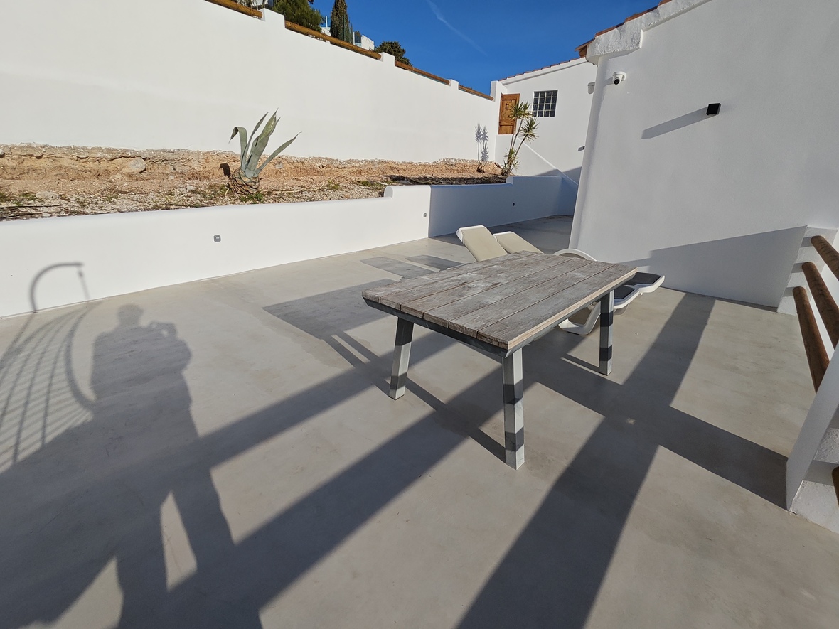 Outdoor terrace with microcement flooring, featuring a weathered wooden dining table and white perimeter walls.