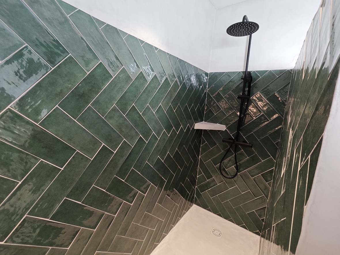 Shower area featuring glossy green tiles in a herringbone layout, contrasted by matte black fixtures and a clean white floor tray.