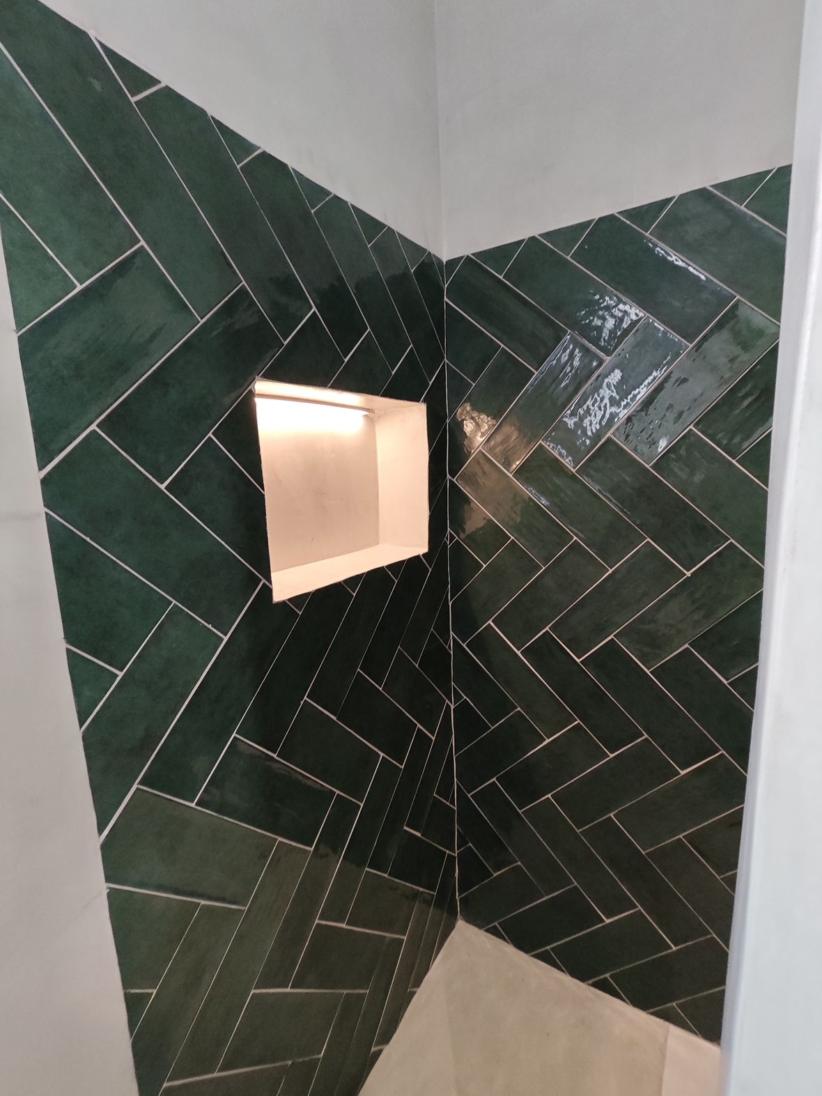 Shower corner detail featuring glossy emerald green tiles in a herringbone pattern and a recessed wall niche with integrated warm lighting.