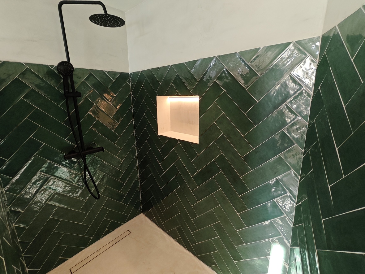 Shower featuring emerald green herringbone tiles, matte black fixtures, and a recessed niche with warm LED lighting. Includes a light-toned floor with a linear drain.