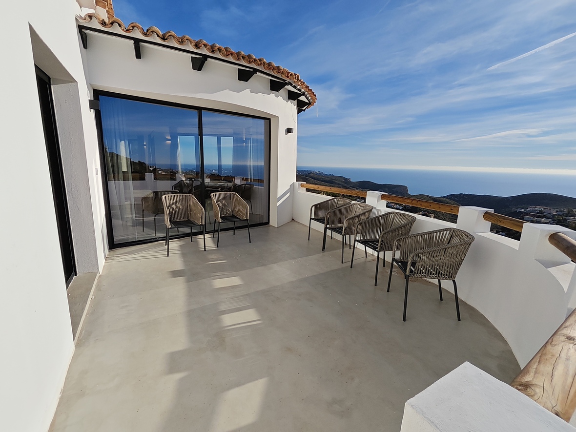 Spacious curved terrace with microcement flooring, woven seating, and panoramic Mediterranean Sea views framed by a white facade and wooden railings.