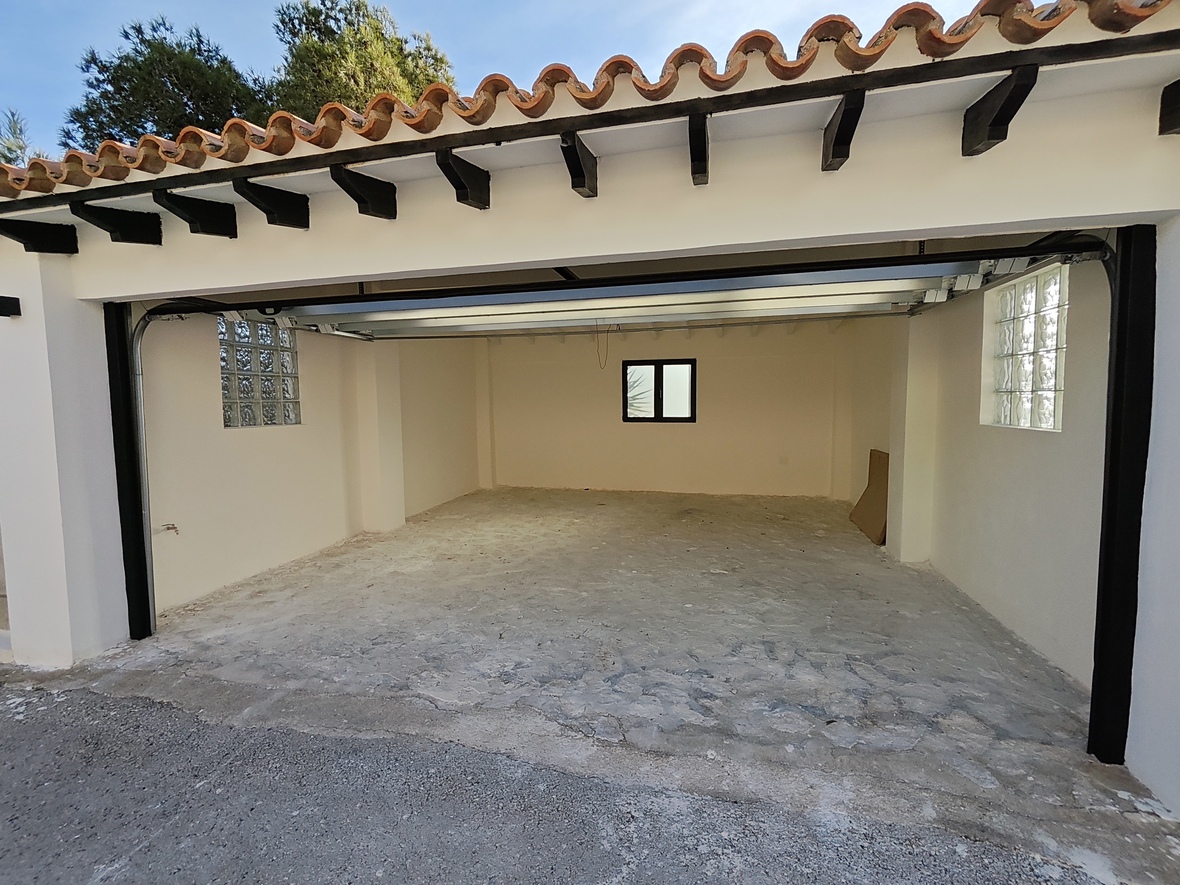 Spacious garage with concrete flooring, featuring glass block windows for natural light and a traditional tiled roof with dark wooden beams.