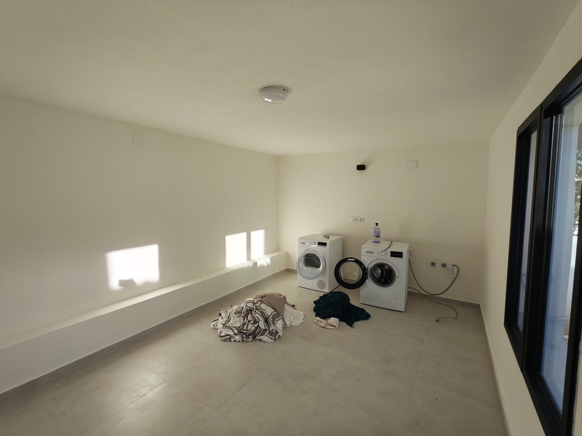 Spacious laundry room featuring a washing machine and dryer, neutral tiled flooring, and natural light from a large side window.
