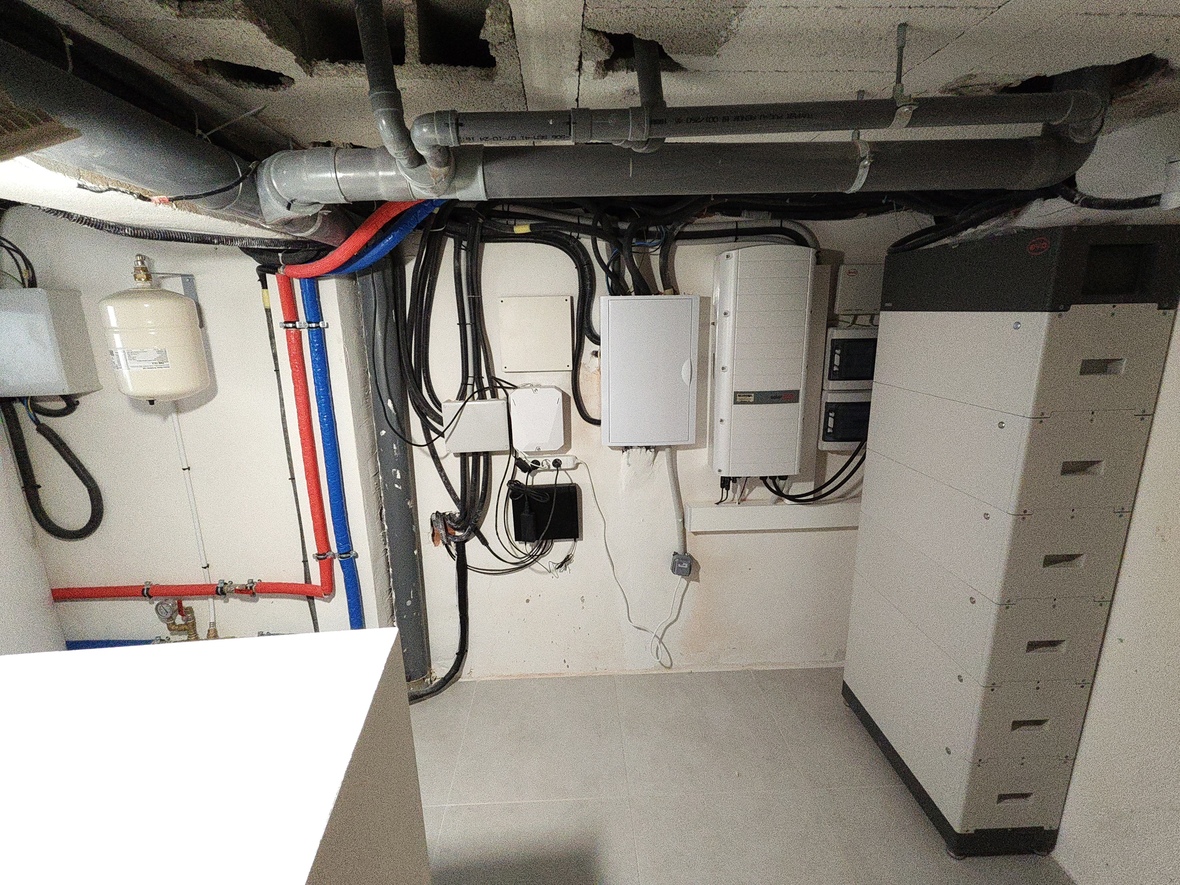 Technical room featuring a SolarEdge inverter, BYD battery storage system, and organized plumbing with an expansion tank and color-coded PEX piping.