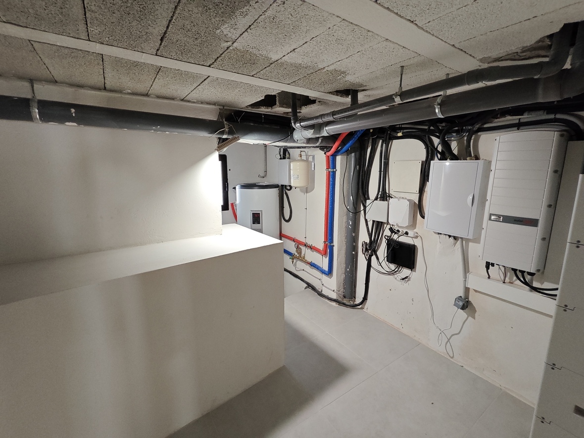 Technical room featuring a SolarEdge inverter, electrical control panels, and a water heating system with integrated PEX piping and drainage.