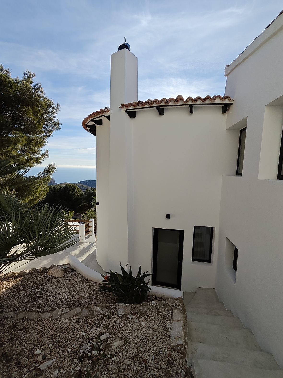White villa exterior featuring a prominent chimney, terracotta roof tiles, and stone stairs leading to the entrance with expansive sea views.