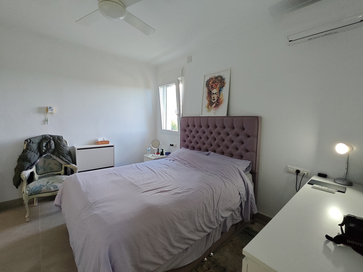 Bedroom featuring a mauve tufted headboard, white walls, a ceiling fan, and a functional workspace with a desk and natural light.