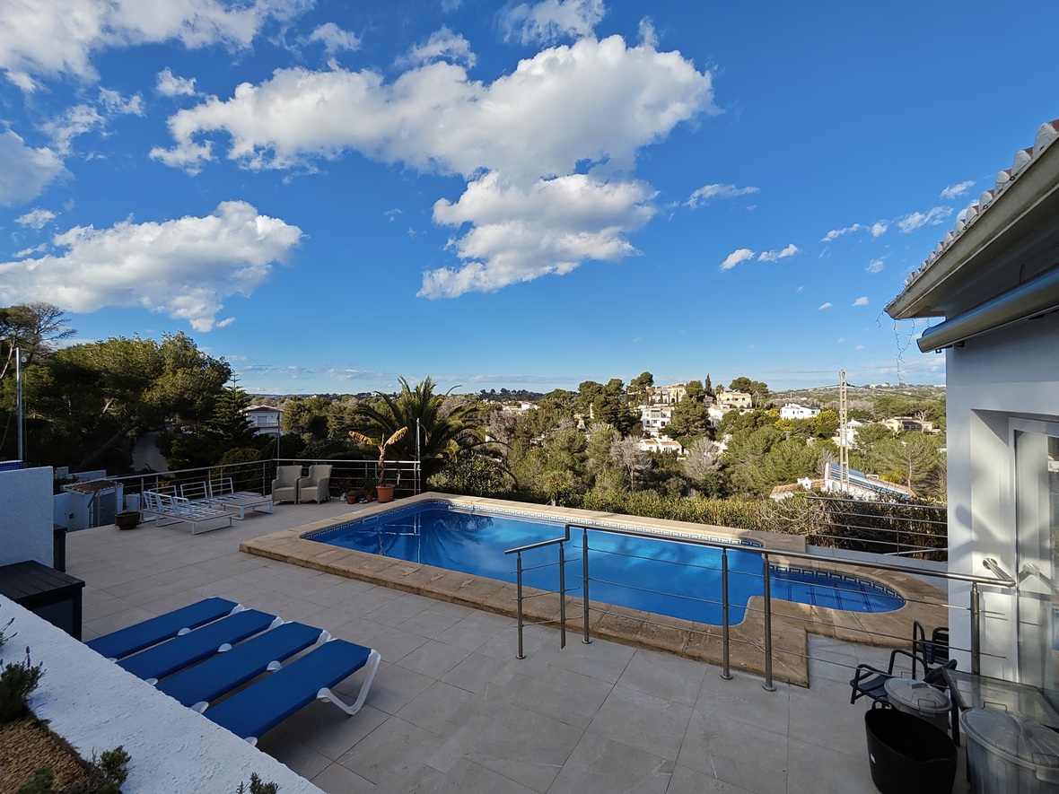 Elevated terrace featuring a rectangular pool with stone coping, blue sun loungers, and panoramic views of the surrounding pine-covered valley.