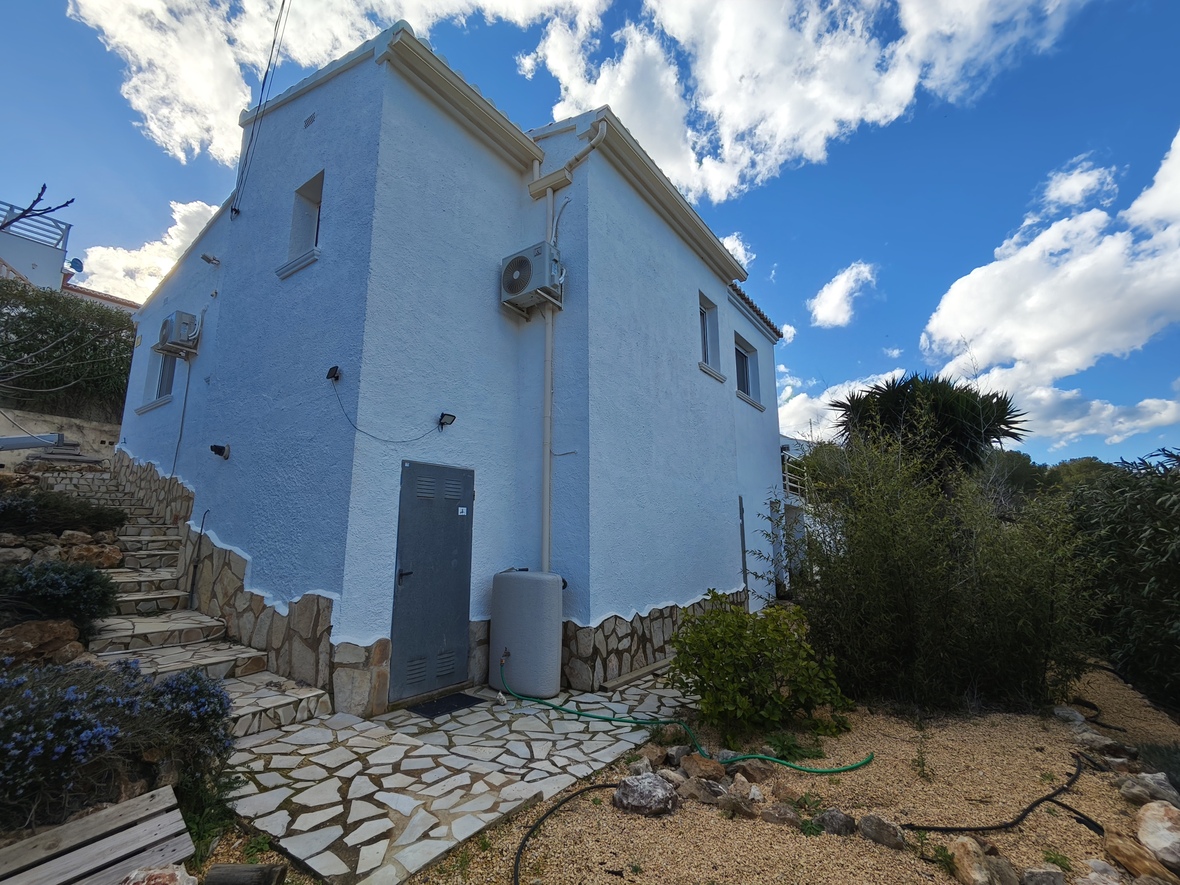 Exterior facade featuring textured white walls, a stone masonry base, and side access. Includes integrated stone stairs and wall-mounted air conditioning units.