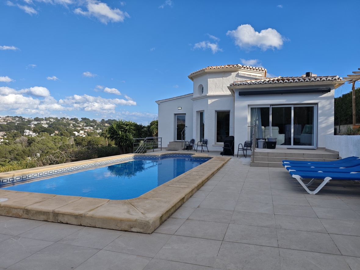 Exterior terrace featuring a rectangular swimming pool with stone coping, blue sun loungers, and views of the surrounding hills.