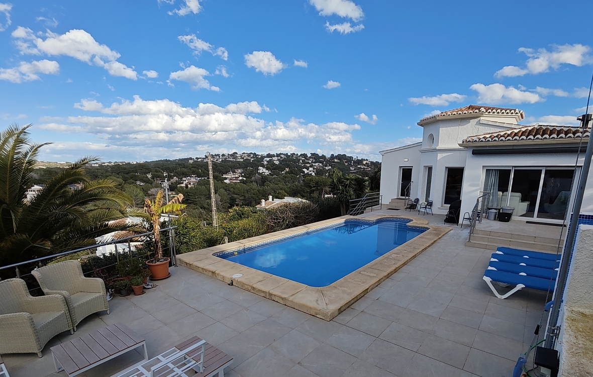 Exterior terrace featuring a rectangular swimming pool with stone coping, sun loungers, and panoramic views over a Mediterranean valley and residential hills.