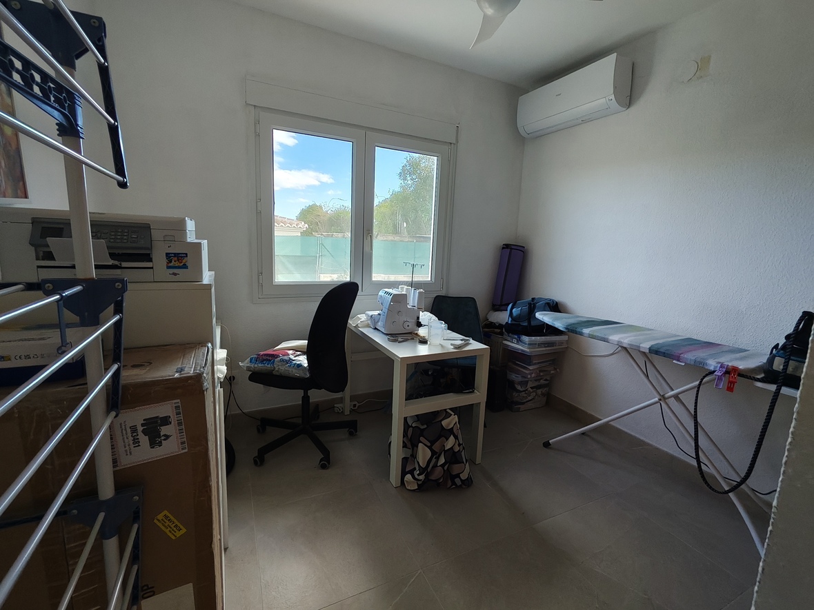 Functional utility room featuring a white desk with sewing equipment, an ironing area, and split-system air conditioning. A double window provides natural light.