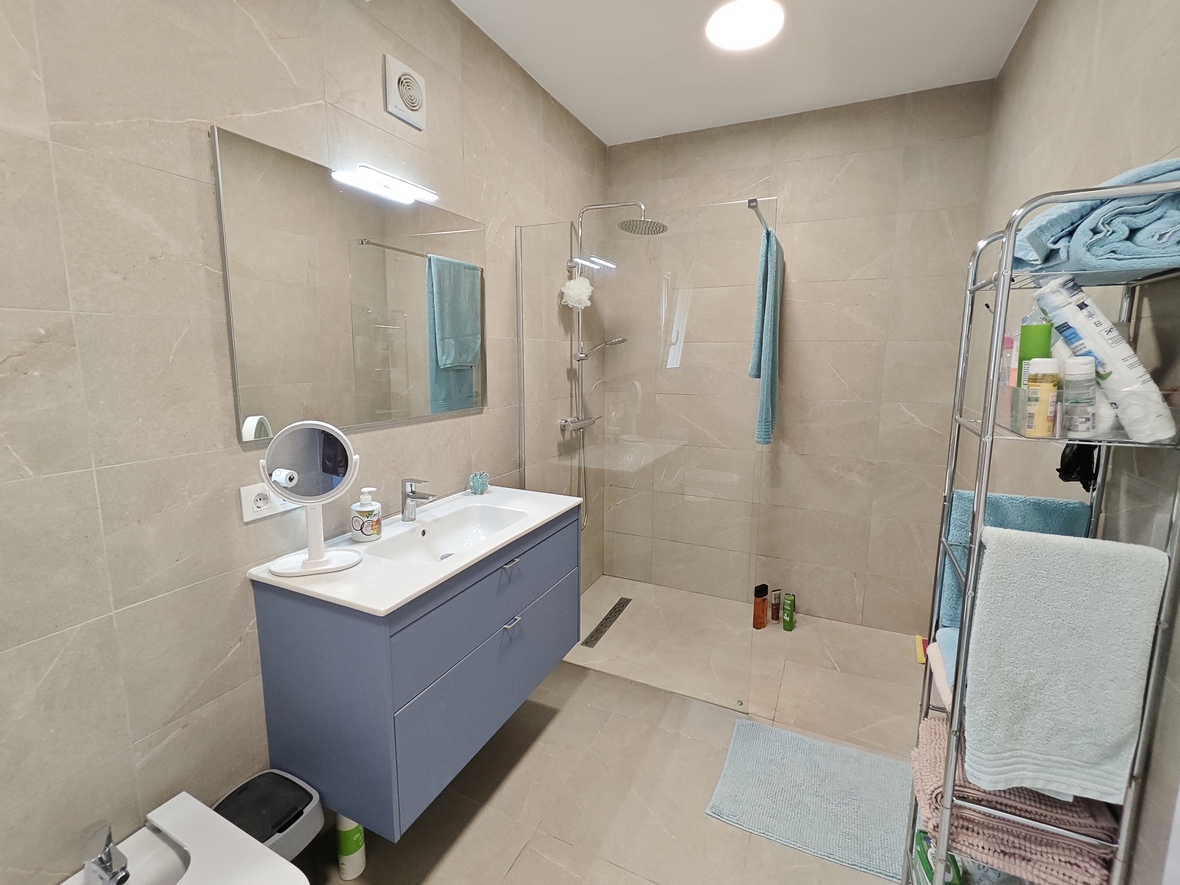Modern bathroom featuring a blue floating vanity, a large walk-in shower with glass partition, and sand-toned ceramic tiling throughout.